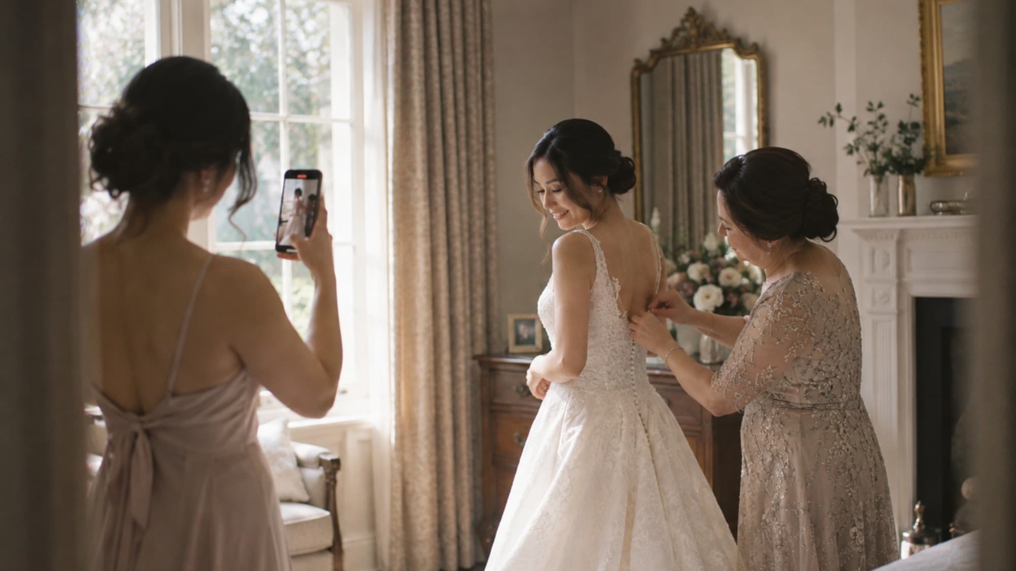 A bridesmaid films the bride getting ready on her phone